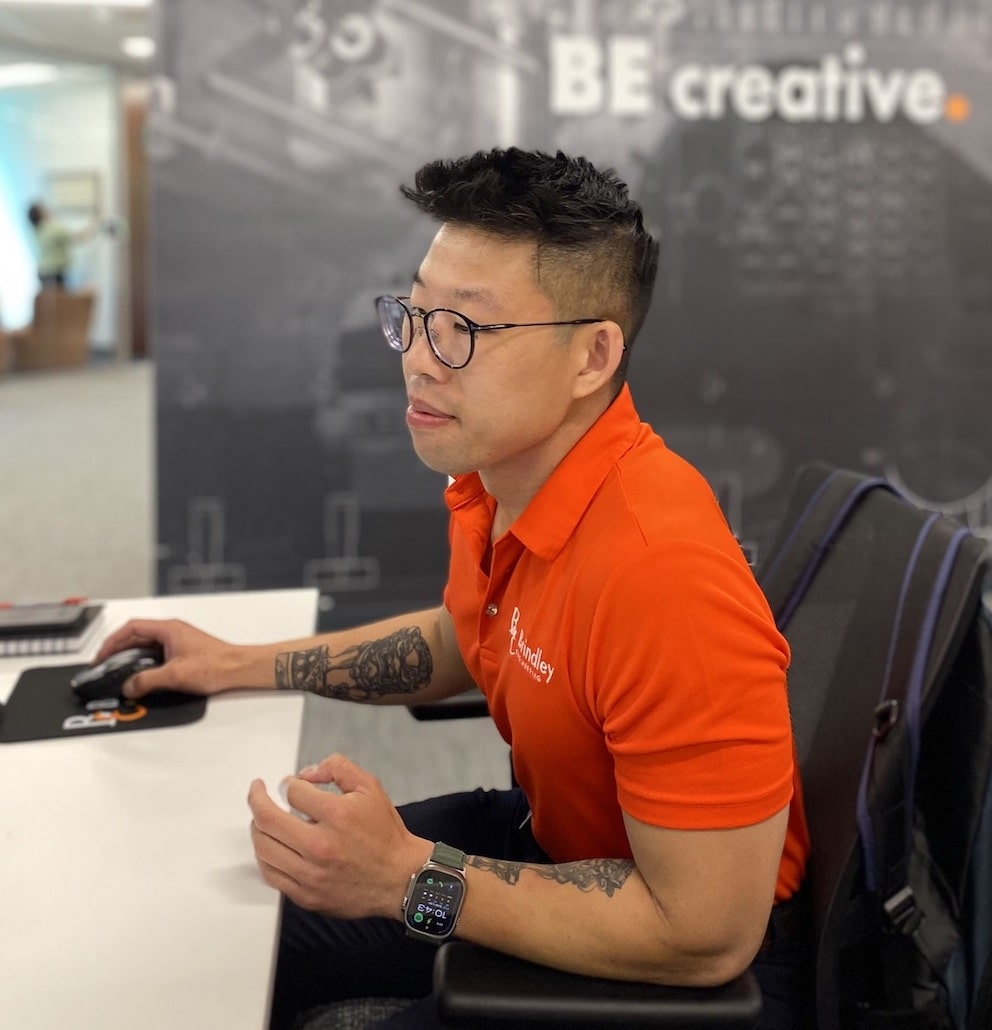 Brindley Engineering team member at desk with BE creative wall decal in background